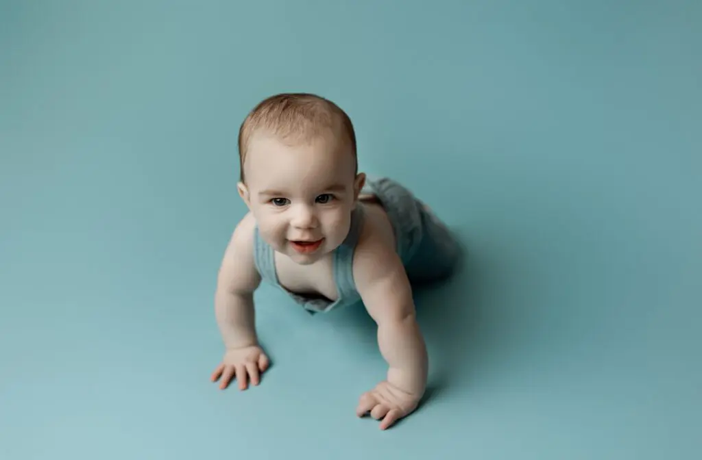 Baby Easton crawling on a blue background, smiling during his 6-month milestone photography session