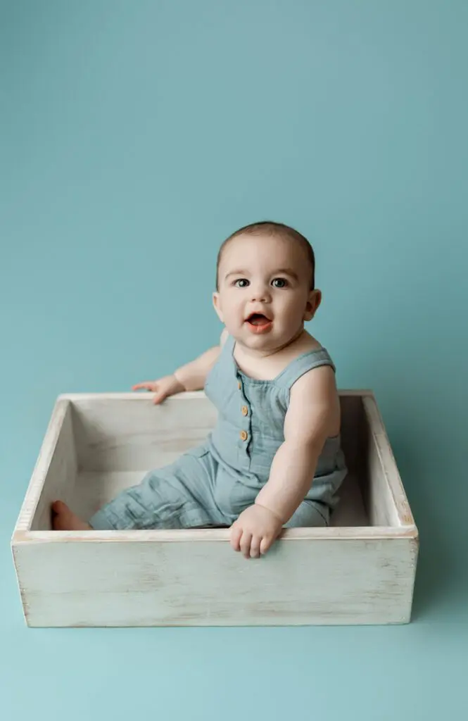 Baby Easton sitting in a white wooden box wearing a blue outfit during his 6-month milestone photography session.