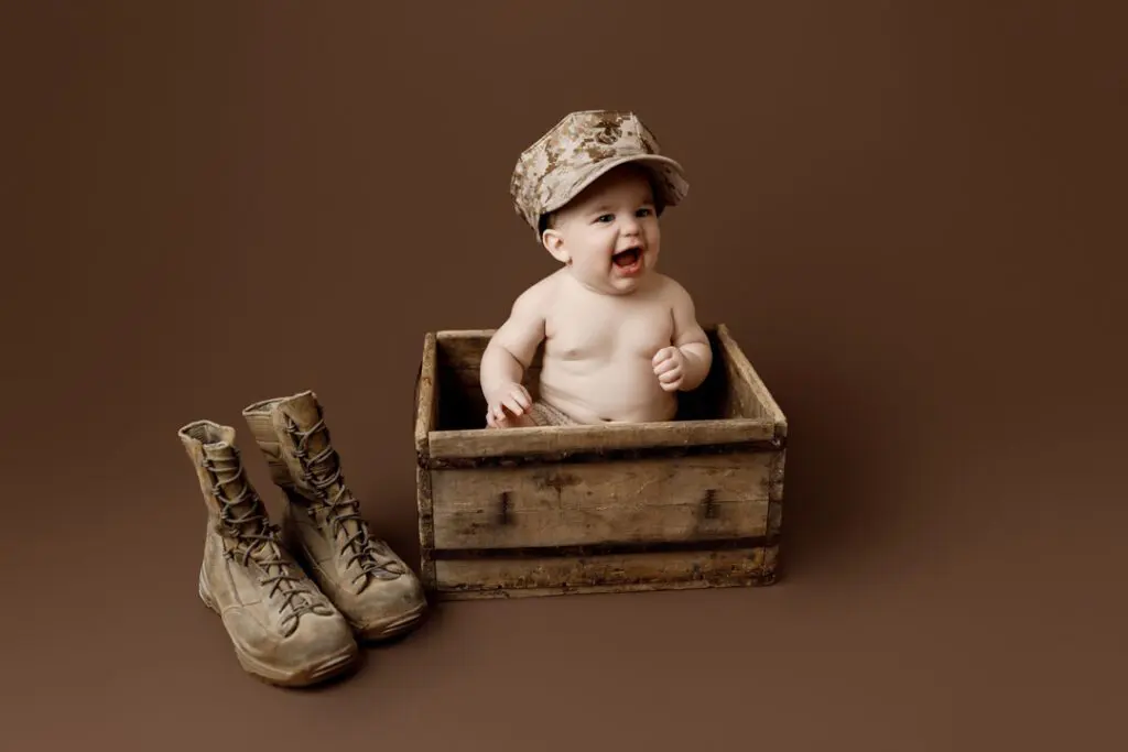 Baby Easton wearing a Marine cap and sitting in a wooden box with Marine boots nearby during a milestone session