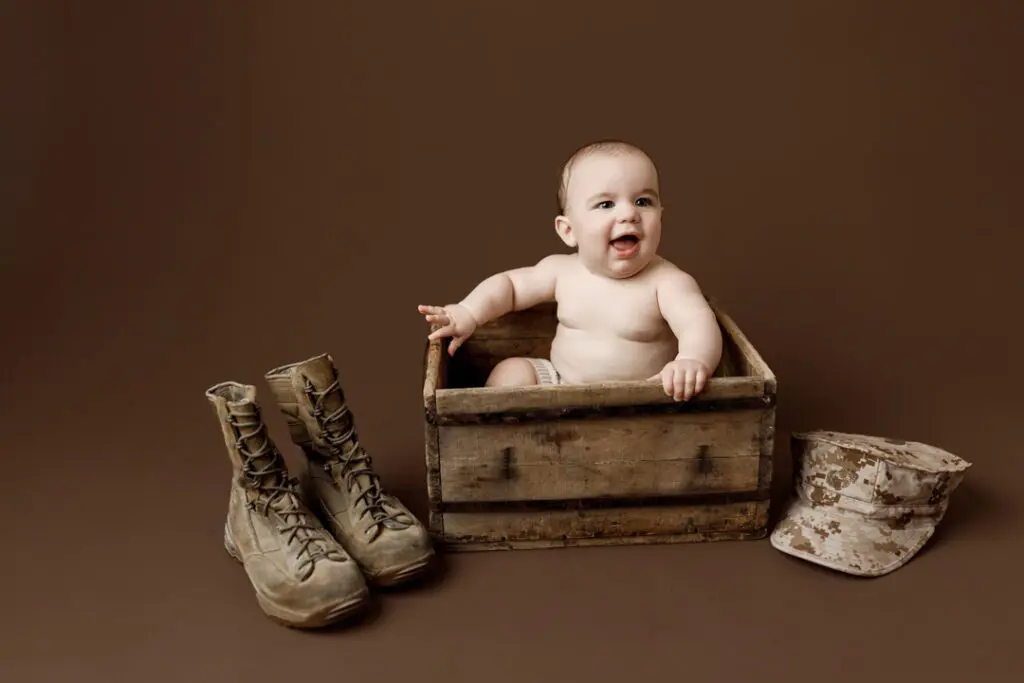 Baby Easton sitting in a wooden box surrounded by Marine boots and a cap during a 6-month milestone session
