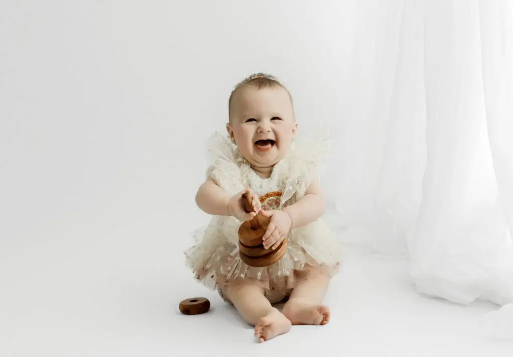 Baby Eyla smiling and playing with wooden toys in a ruffled dress during her 6-month milestone session