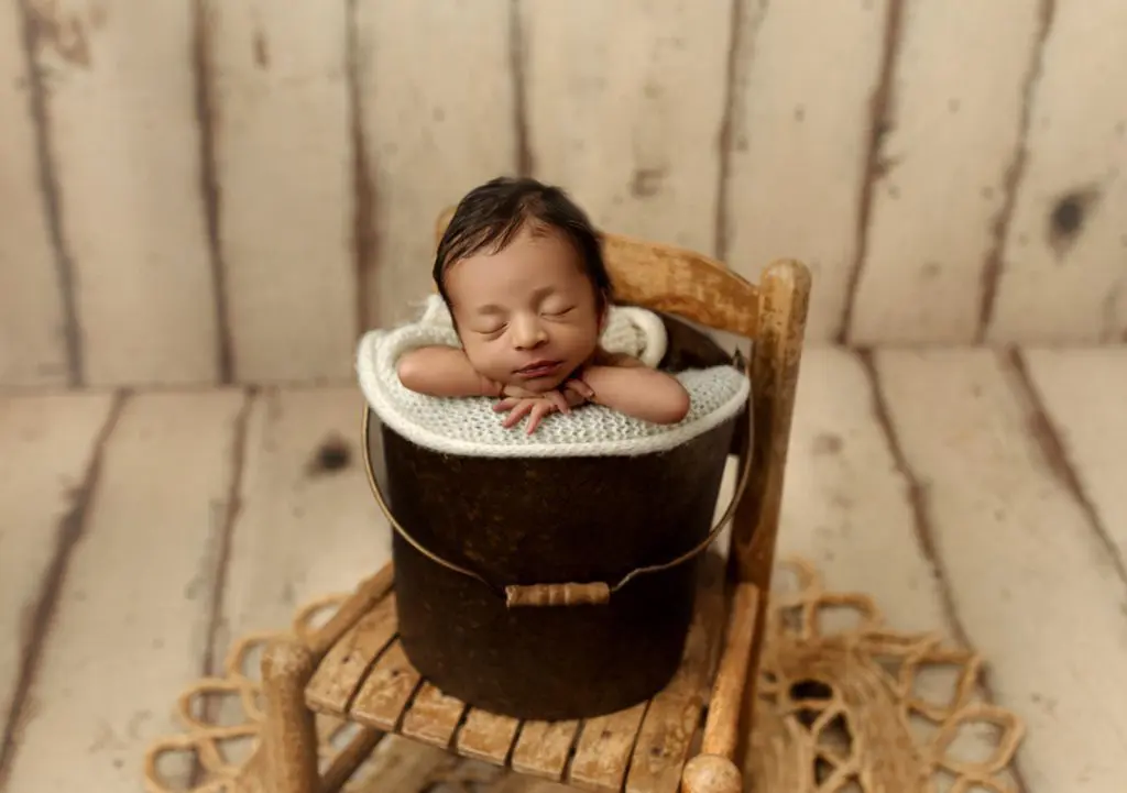 Newborn baby Isaiah posed in a rustic bucket on a wooden chair, surrounded by warm tones, during a Cedar Falls photography session.