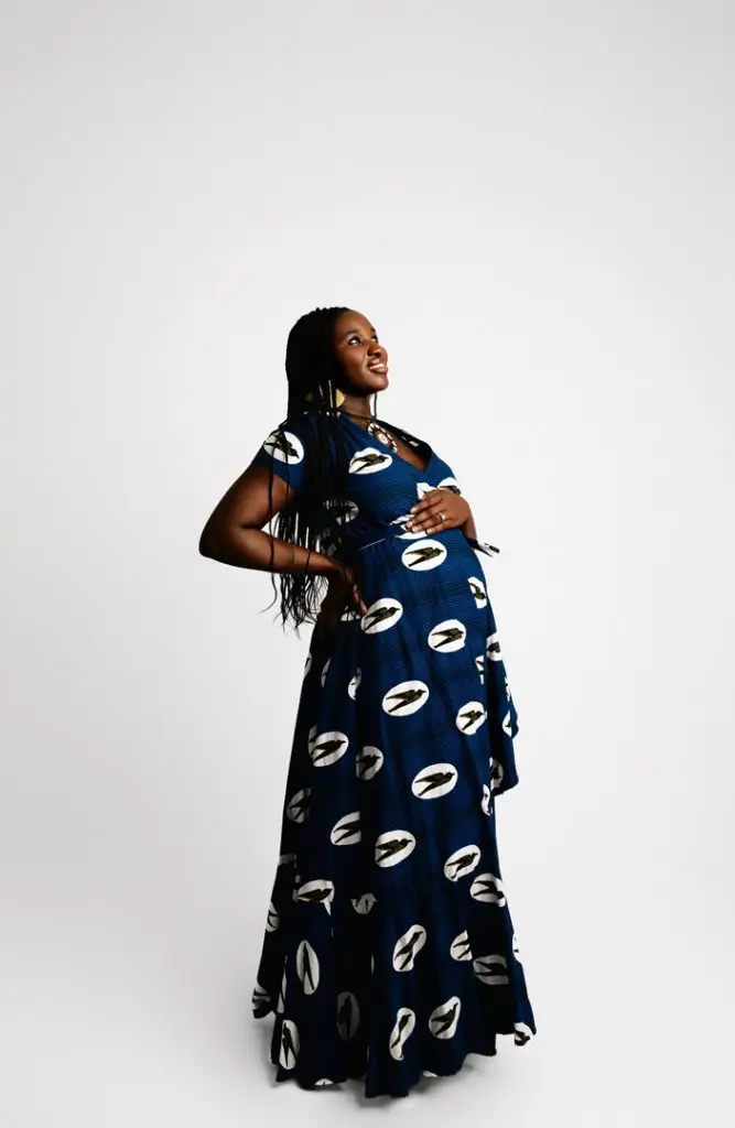 Pregnant woman wearing a bold blue patterned maternity dress, smiling confidently in a bright studio setting, ideal for maternity photography in Cedar Falls, Waterloo, and Hudson, Iowa