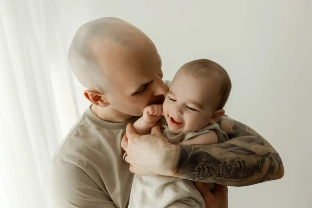 A father holding and kissing his happy 6-month-old baby, Easton, during a milestone session