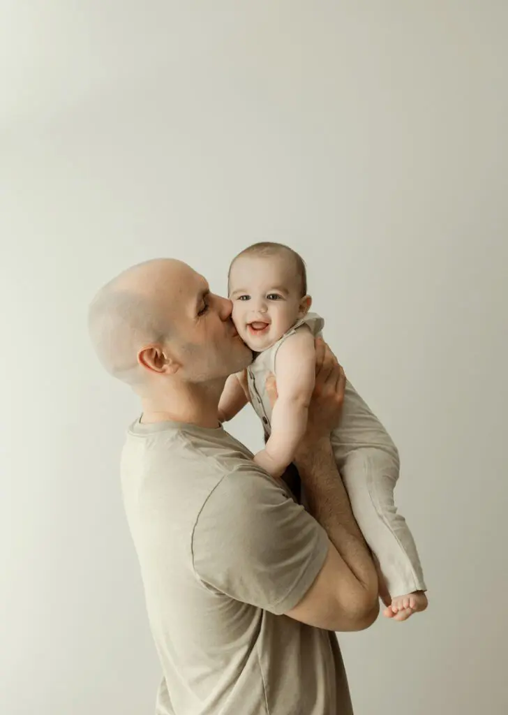 A father kissing his smiling 6-month-old baby, Easton, during a milestone photography session.