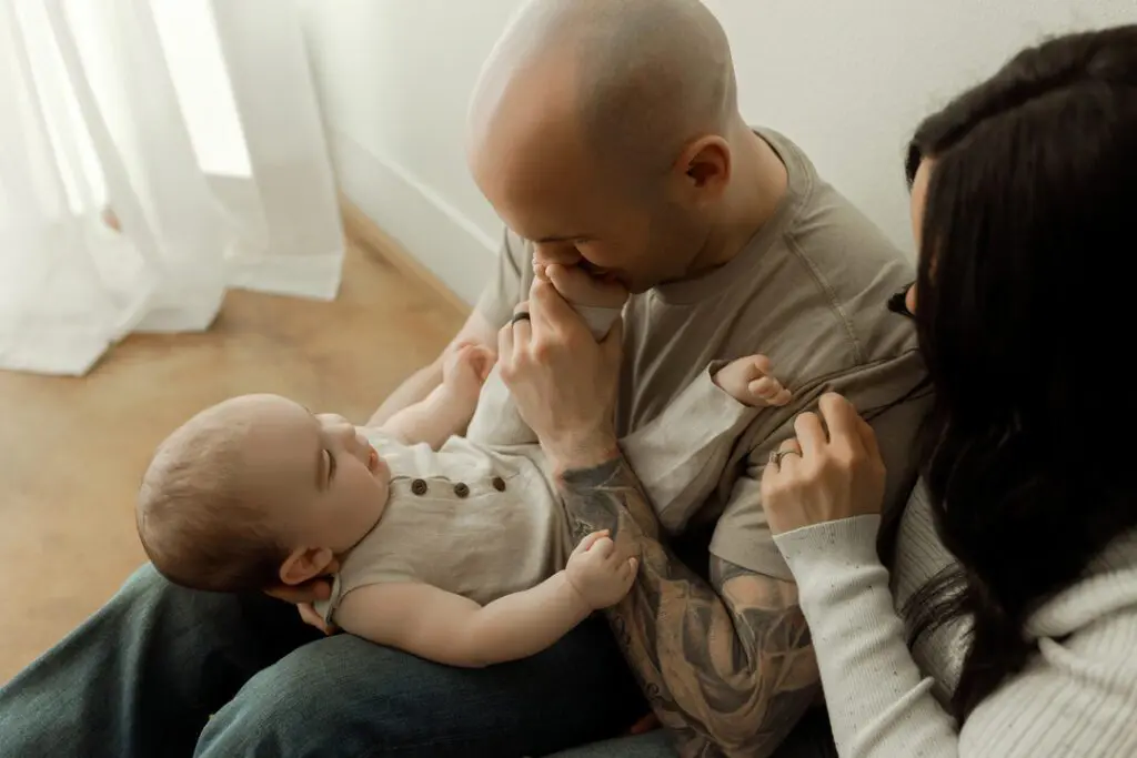A father kissing his baby Easton's feet while the mother looks on lovingly during a milestone session