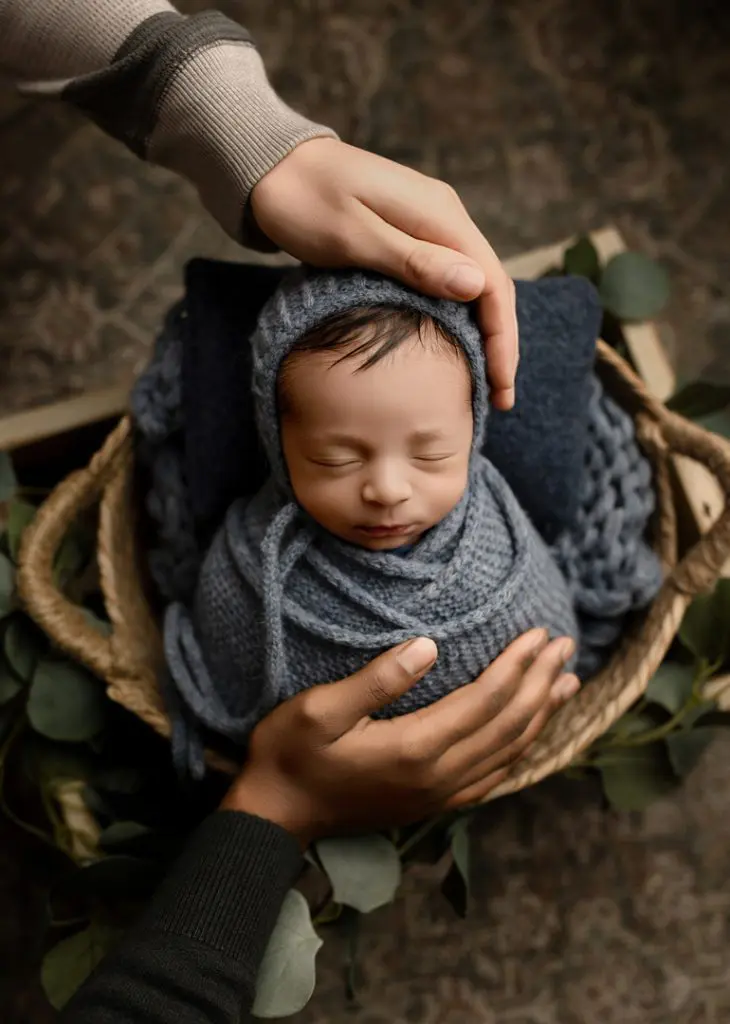 A touching moment of family hands cradling baby Isaiah, wrapped in a soft gray knit, during a Cedar Falls newborn photography session.
