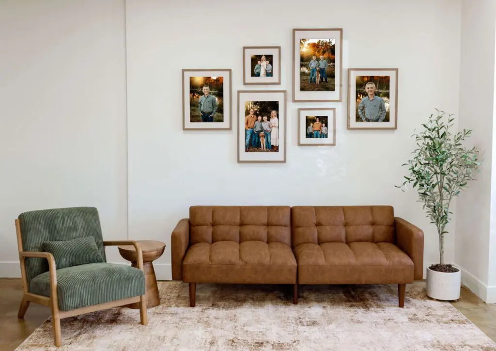 A modern living room wall gallery featuring framed family portraits near Waverly, Iowa. The arrangement includes a mix of individual and group photos, complemented by a leather sofa, a green accent chair, and a potted plant
