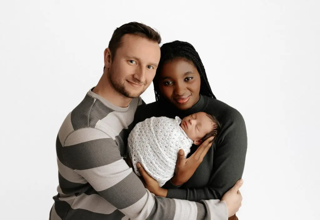 A beautiful family portrait featuring baby Isaiah wrapped in a white knit blanket, held lovingly by his parents during a Cedar Falls newborn photography session.