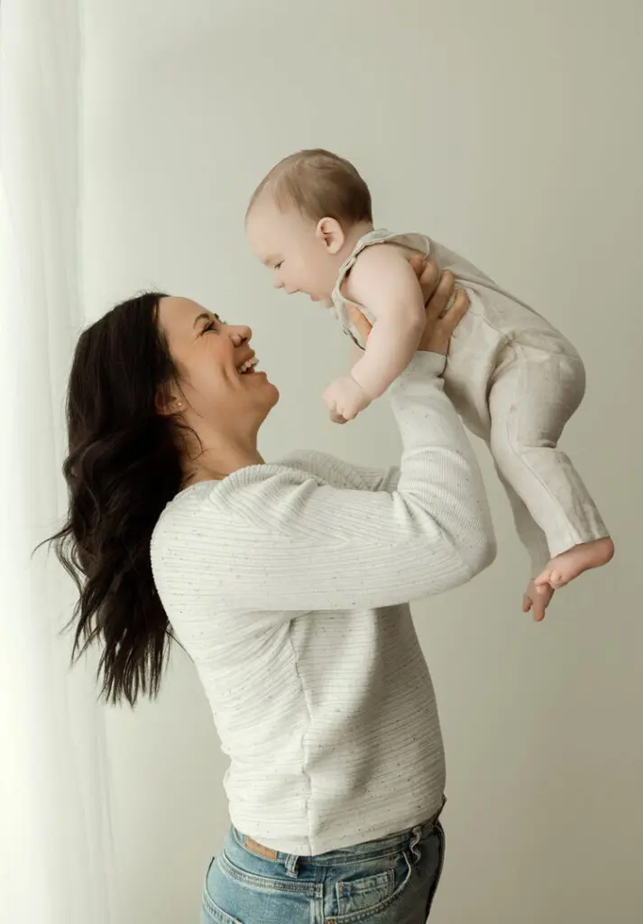 A mother lifting her smiling 6-month-old baby, Easton, during a milestone photography session