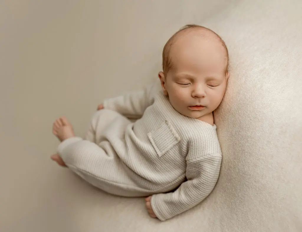 A serene newborn baby dressed in a cream-colored outfit, resting peacefully during a photography session in Cedar Falls, Iowa. Ideal for families in Cedar Falls, Waterloo, and surrounding areas