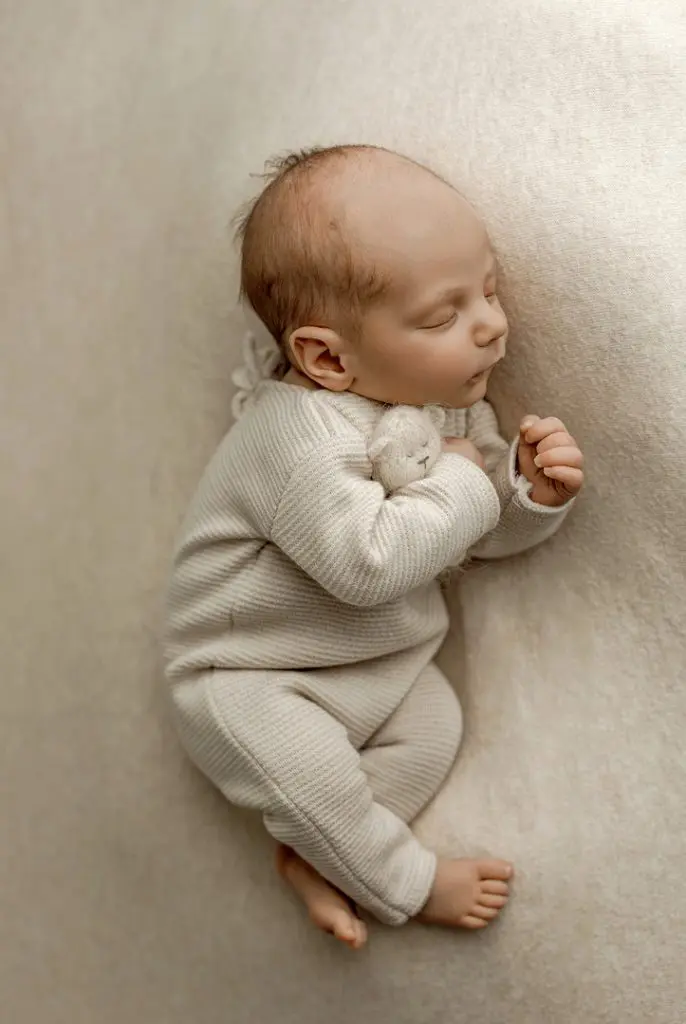 A peaceful newborn baby sleeping while holding a small teddy bear, captured during a professional photography session in Cedar Falls, Iowa. Perfect for families in Cedar Falls, Waterloo, and Waverly