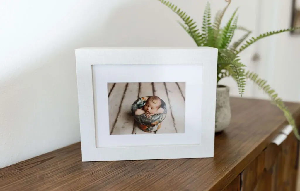 Framed newborn portrait displayed on a wooden cabinet at Little Moments by Sarah Photography Studio in Cedar Falls, Iowa. Ideal for families in Cedar Falls, Parkersburg, Shell Rock, and Reinbeck.