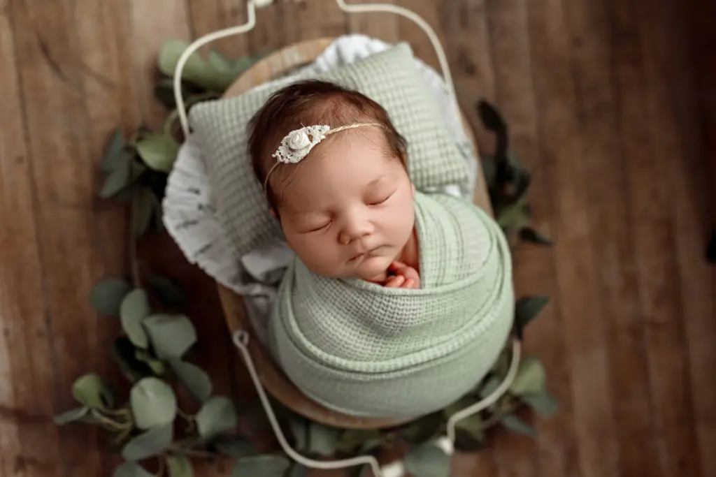 Baby wrapped in mint green swaddle posed with eucalyptus during Cedar Falls newborn session.