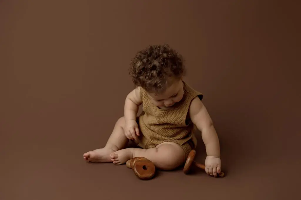 Adorable baby playing with a wooden rattle on a neutral backdrop during a newborn photography session near Waterloo, Iowa.