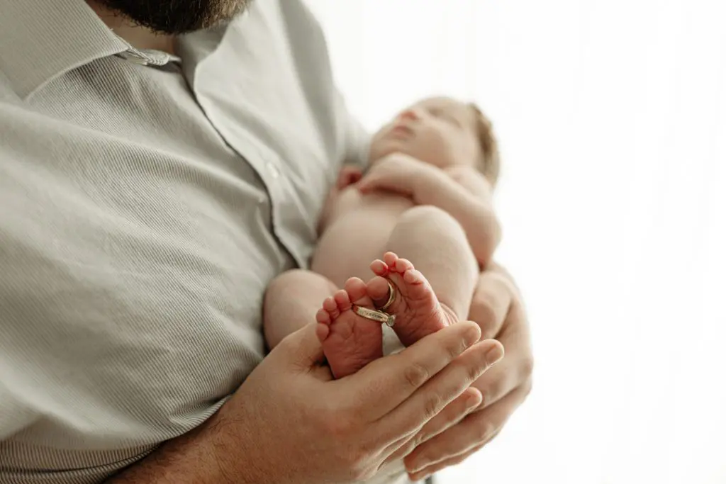 Newborn baby’s tiny feet adorned with grandmother's wedding rings during sentimental Cedar Falls photo session.