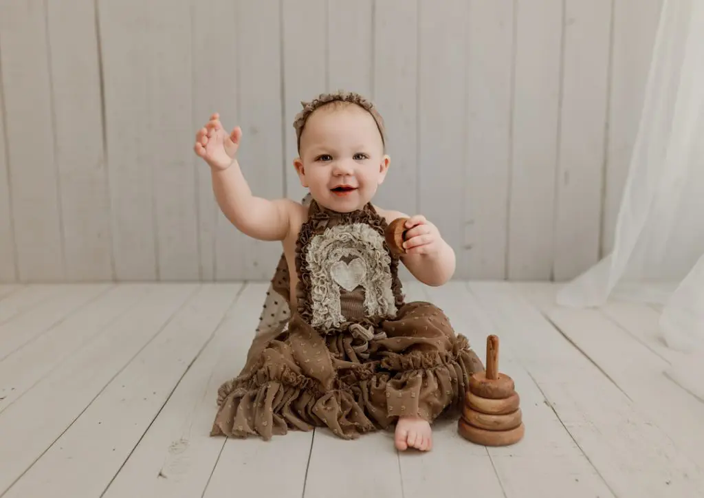 Cheerful baby waving during her playful studio milestone photography session near Denver, IA.