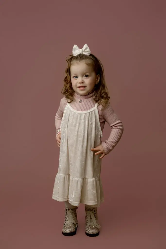 Mabel smiling in a pink sweater and white dress during her mini session as the cutest baby contest winner