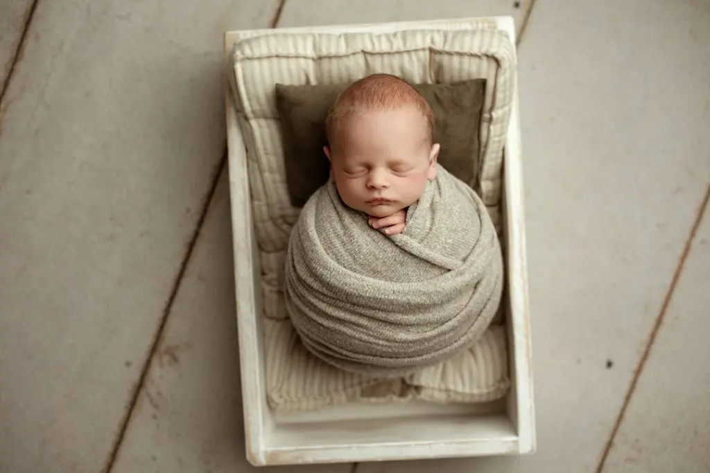 Newborn baby Hudson swaddled and sleeping in a wooden crate.