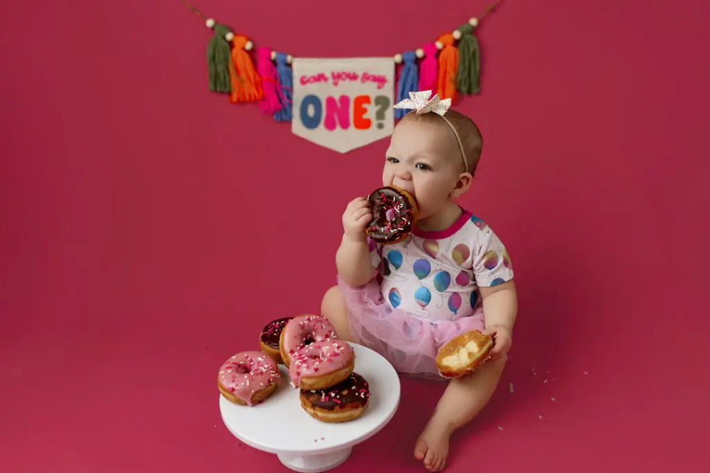 Baby girl enjoying donut-themed cake smash session near Waterloo, Iowa.