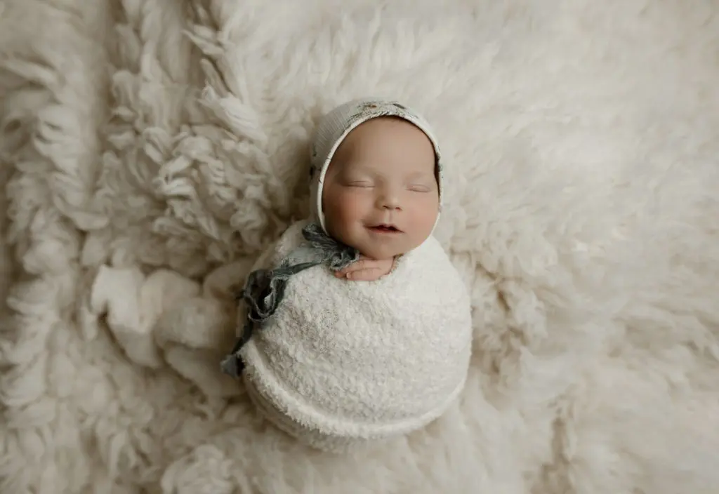 Smiling newborn in custom wrap and bonnet during Waterloo, IA newborn session.