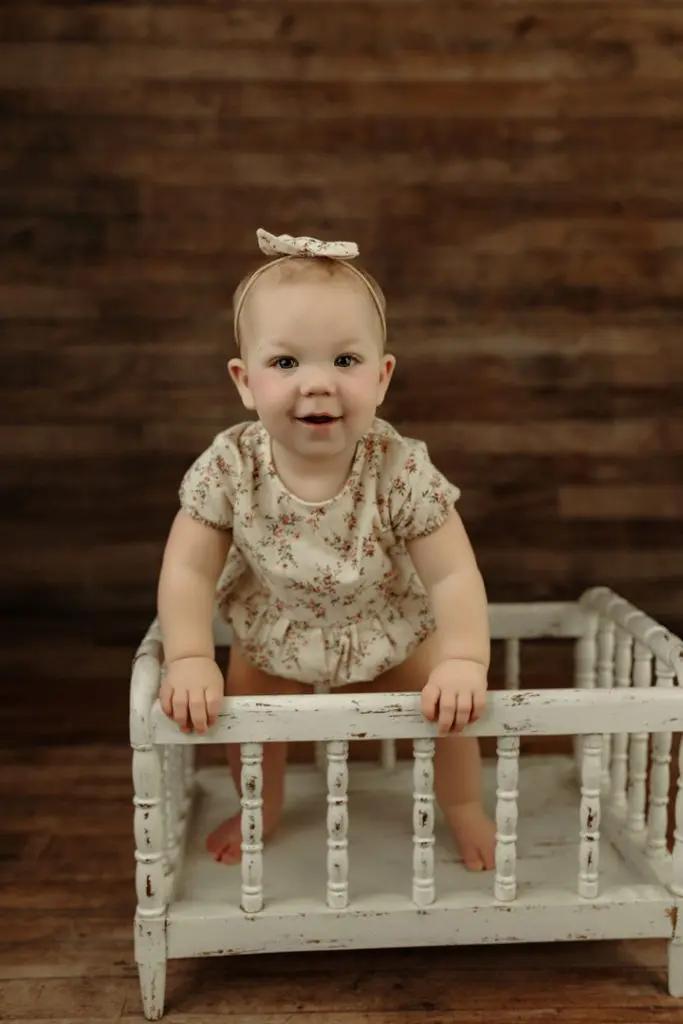 Adorable baby girl standing and smiling during milestone session near Waverly, IA.