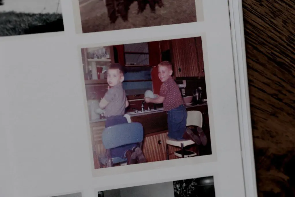 Two young boys doing dishes at the kitchen sink in a candid vintage photo.
