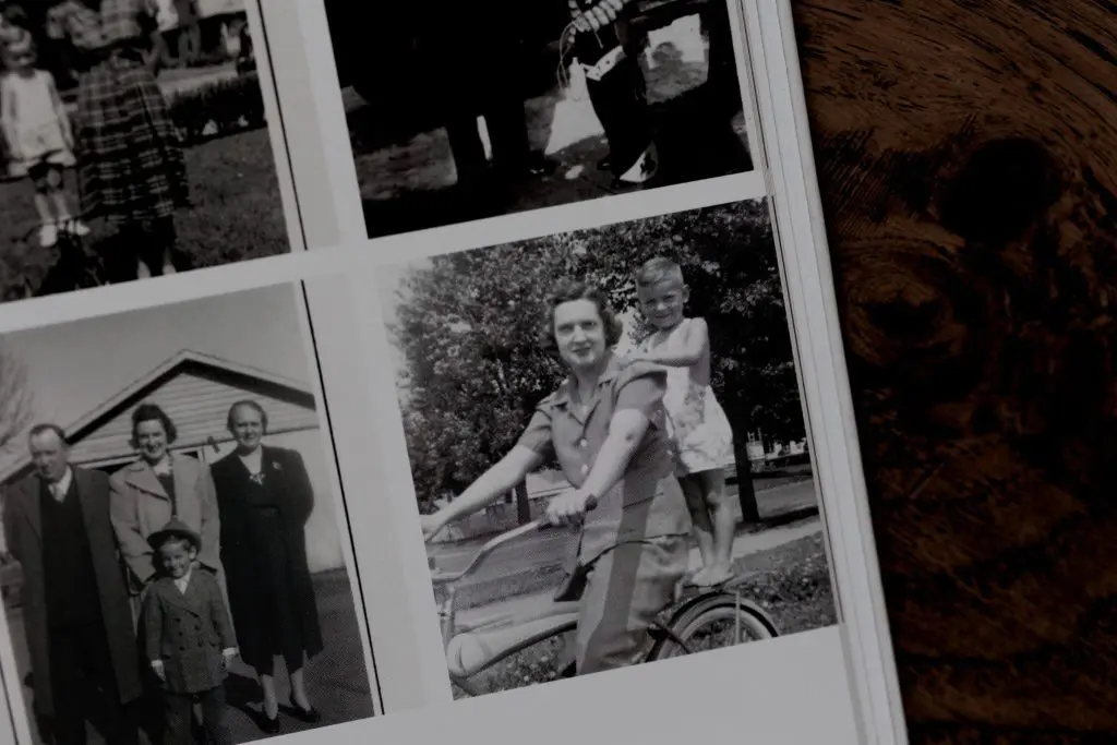 Grandmother riding bicycle with child standing on the back in black and white vintage photo.