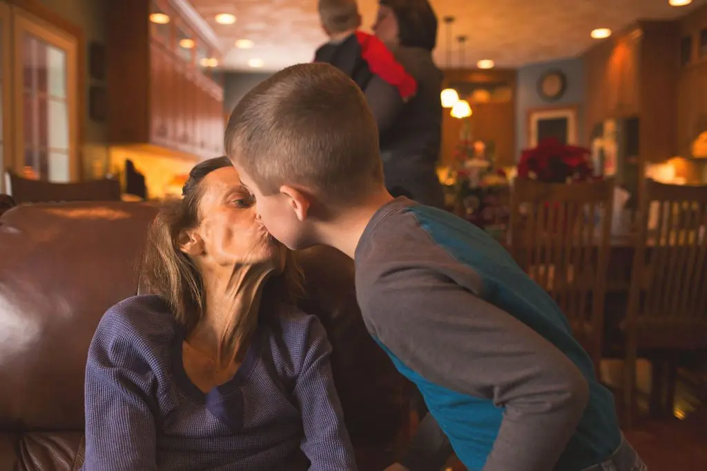 Young boy leaning in to kiss his terminally ill grandmother during a heartfelt goodbye.