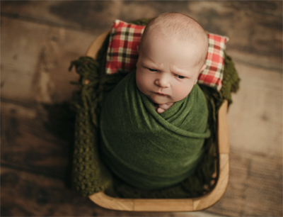 Newborn baby in green swaddle with plaid pillow on wood backdrop – Cedar Falls studio session