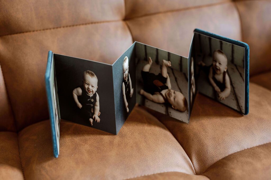 Accordion-style photo album featuring baby portraits, displayed on a leather couch in Cedar Falls, Iowa. Ideal for families in Cedar Falls, Grundy Center, La Porte City, and Denver, Iowa.