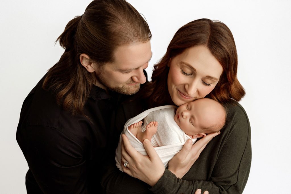 A loving family portrait featuring mom, dad, and their newborn baby wrapped in a cozy swaddle. Captured by a professional photographer in Cedar Falls, Iowa, serving families in Waterloo, Hudson, and surrounding areas