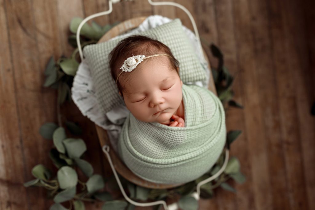 Baby wrapped in mint green swaddle posed with eucalyptus during Cedar Falls newborn session.