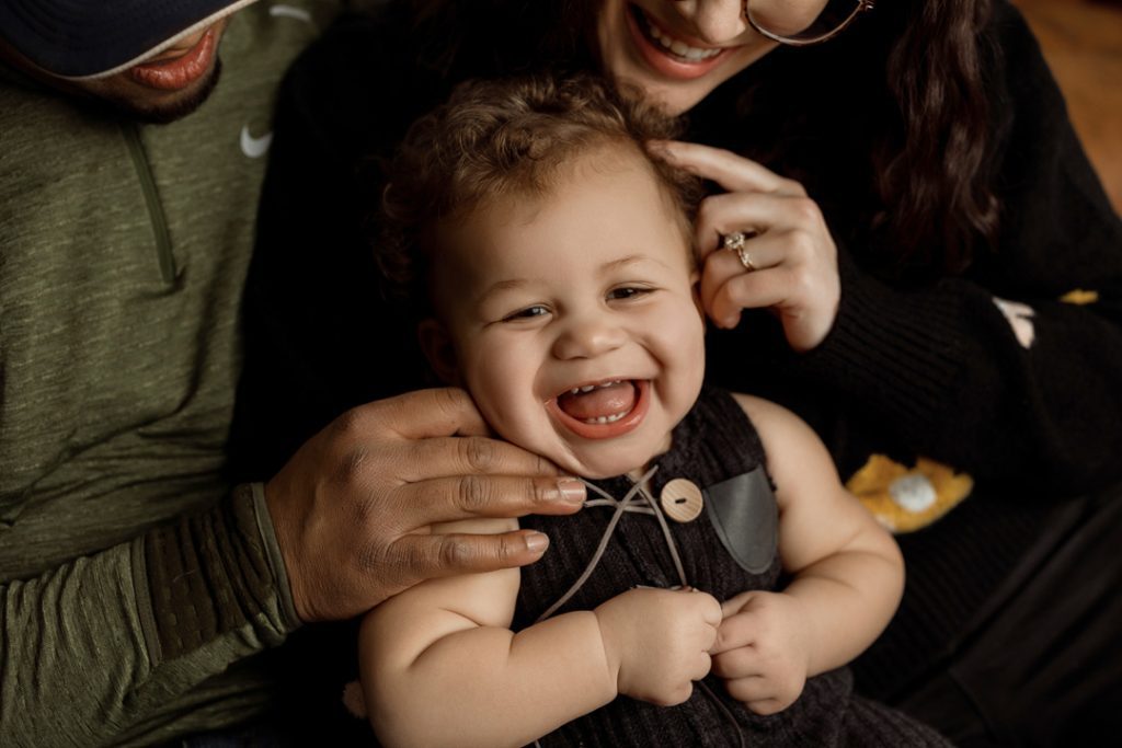 Laughing baby surrounded by loving parents during a family photography session near Waverly, Iowa, capturing heartwarming moments.