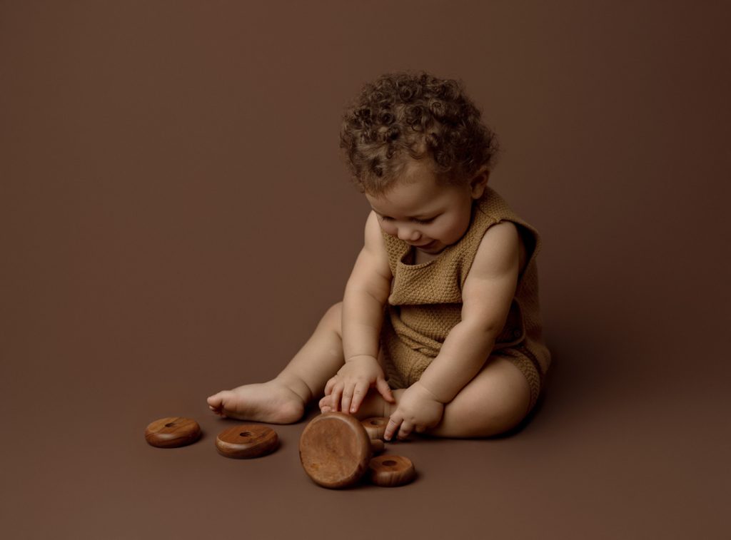Adorable baby playing with wooden toys during a newborn photography session in Cedar Falls, Iowa, showcasing natural and timeless moments.