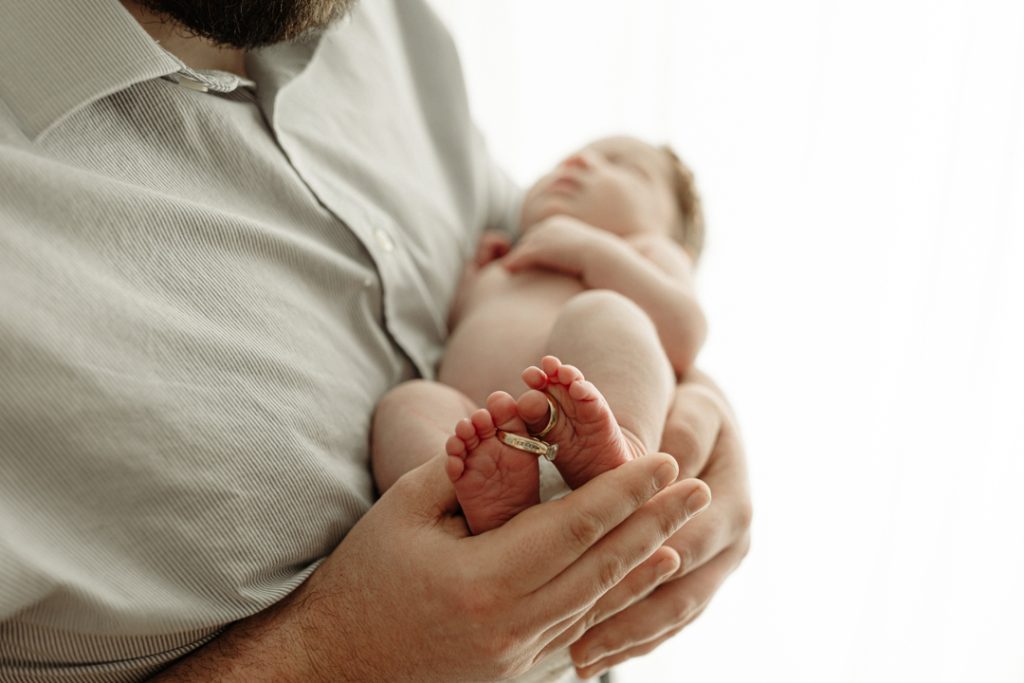 Newborn baby’s tiny feet adorned with grandmother's wedding rings during sentimental Cedar Falls photo session.