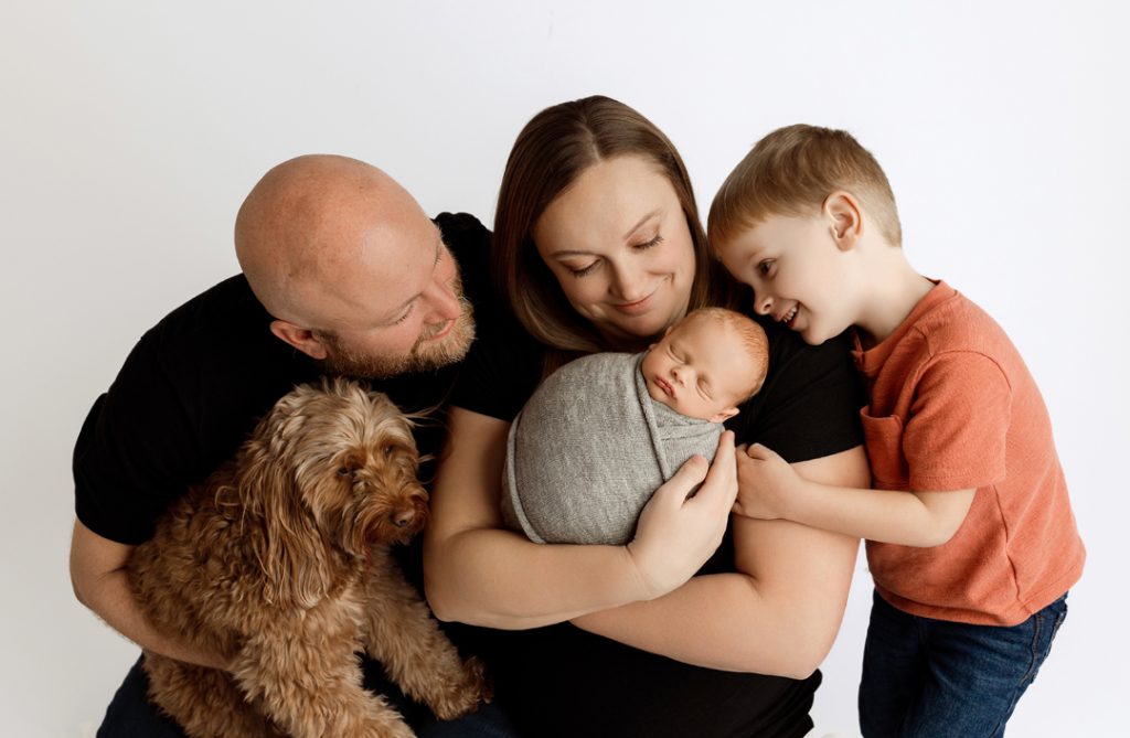 Parents holding newborn baby Hudson with older brother Camdyn and their goldendoodle in Cedar Falls, Iowa.