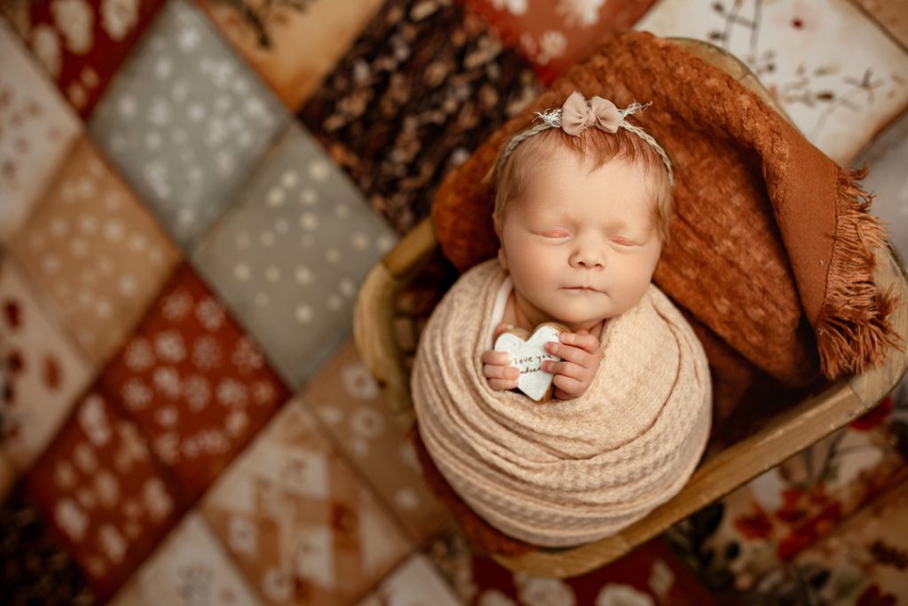 Newborn holding sentimental heart heirloom during professional photo session near Hudson, Iowa.
