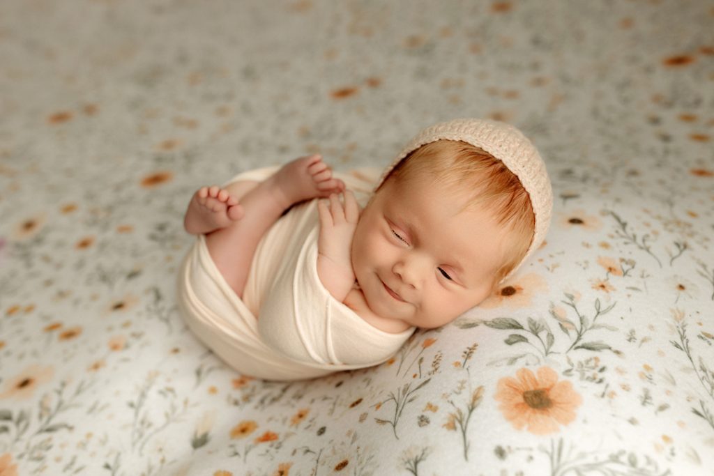 Smiling newborn swaddled in floral wrap, newborn photographer near Waverly, Iowa.