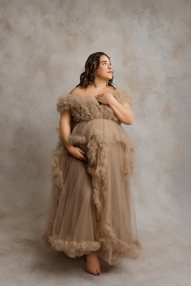 Elegant maternity portrait with neutral ruffled gown captured in photography studio near Denver, IA.