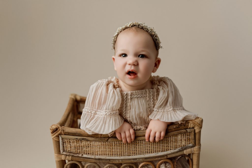 Smiling baby girl in a rustic basket during milestone photography session near Hudson, IA.