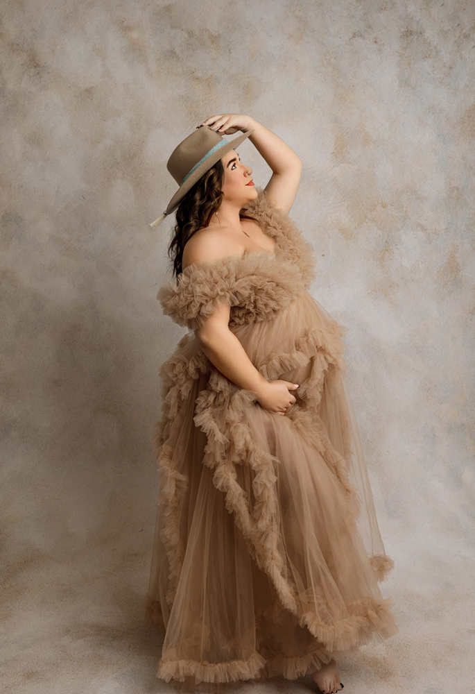 Expectant mother in ruffled gown with western hat during maternity photoshoot near Evansdale, IA.