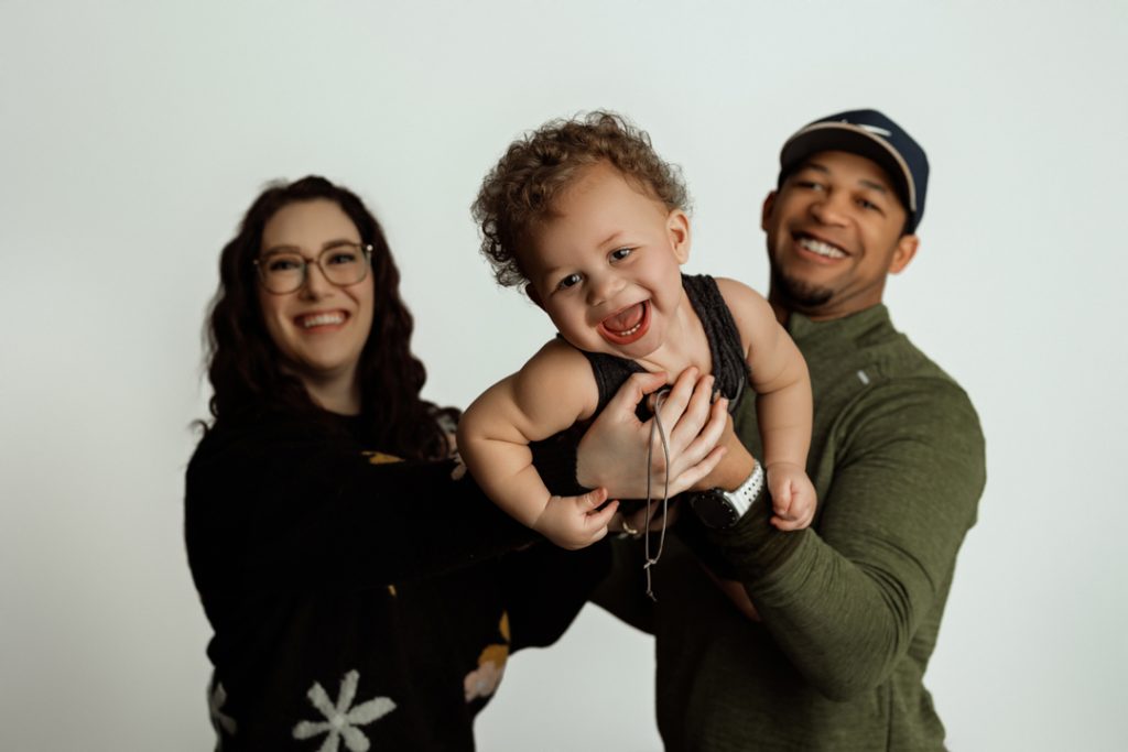 Happy family holding their smiling baby during a newborn and family photography session in Cedar Falls, Iowa, perfect for capturing joyful memories.