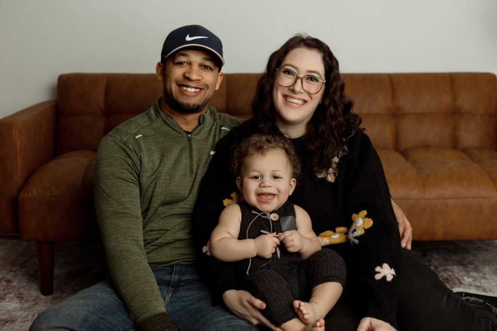 Happy family sitting together on a couch during a one year milestone and family photography session in Cedar Falls, Iowa, showcasing their love and connection.