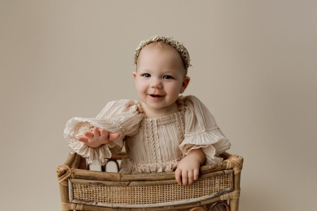 Smiling baby girl in a rustic basket during milestone photography session near Hudson, IA.