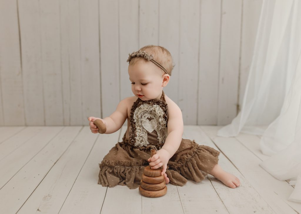Baby girl playing with wooden toys during milestone photoshoot near Evansdale, Iowa.