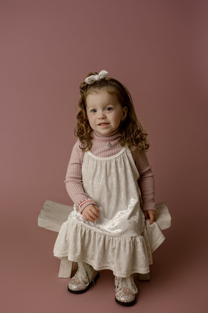 Mabel sitting on a bench in a white dress and sparkly boots during her mini session in Cedar Falls, Iowa.