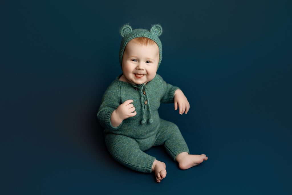 Six-month-old baby in a bear hat romper smiling during milestone session in Cedar Falls.