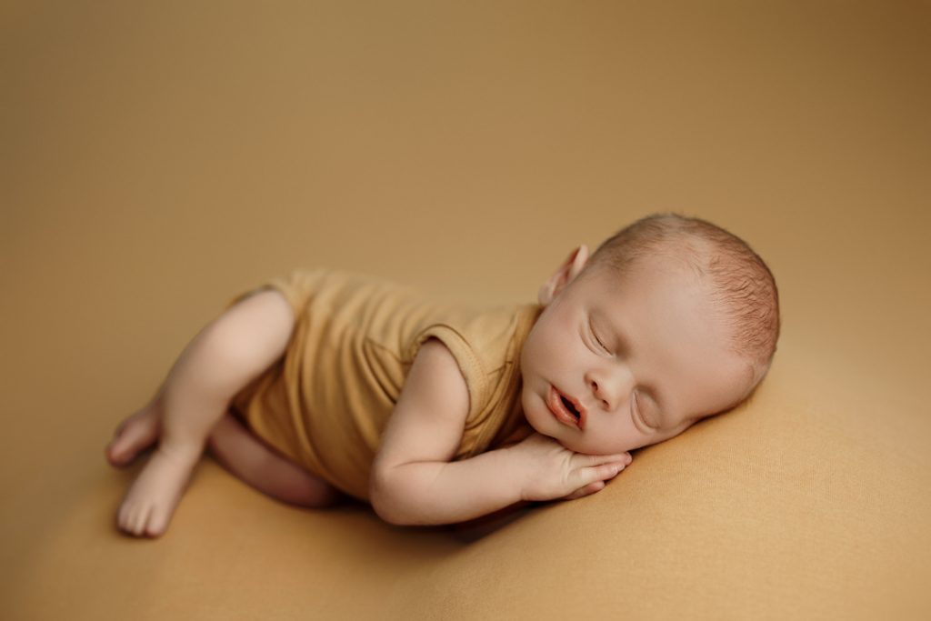 Newborn baby Hudson peacefully sleeping on a mustard backdrop.