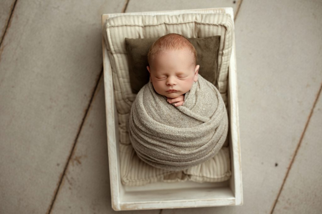 Newborn baby Hudson swaddled and sleeping in a wooden crate.